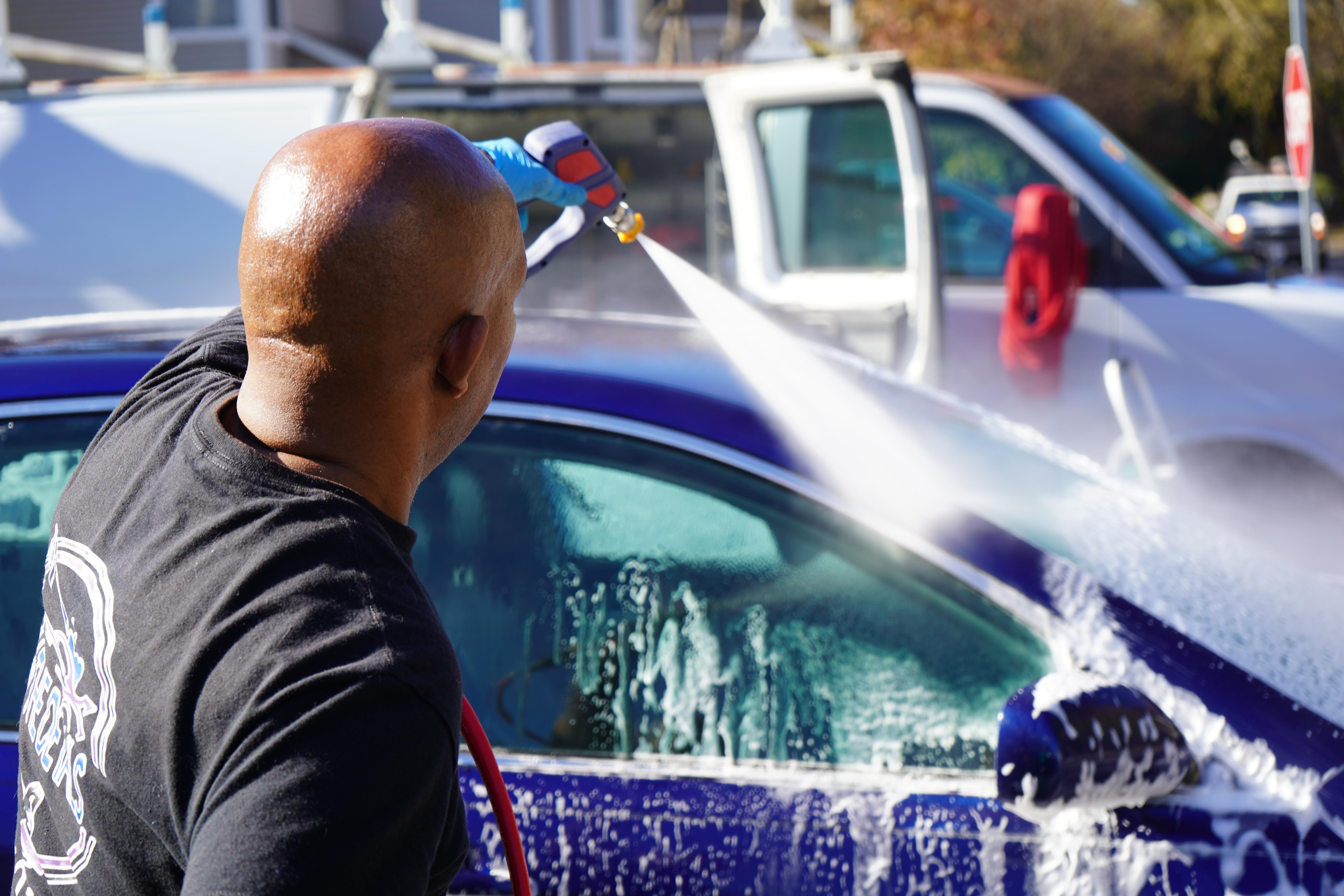 Image depicting the team washing a blue car as the company an its in the backdrop