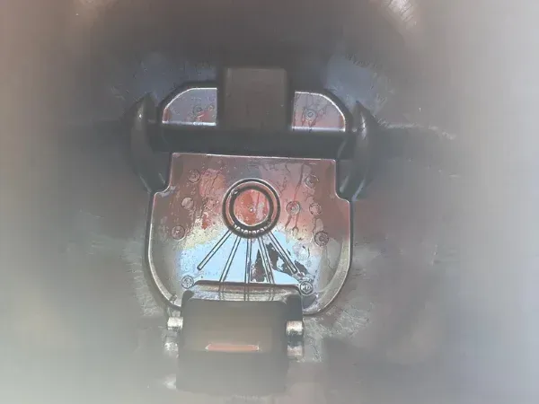 A close-up, top-down view inside a trash can, showing the reflective metallic water spout with water stains.