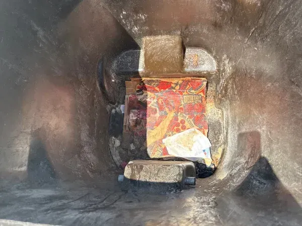 Looking down into a dirty, mostly empty dark grey trash can with a few light reflections and some debris at the bottom.