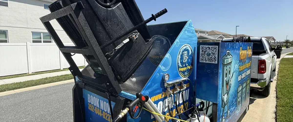 A mobile cleaning trailer with blue Happy Pails branding, showing a bin being lifted on a sunny day.