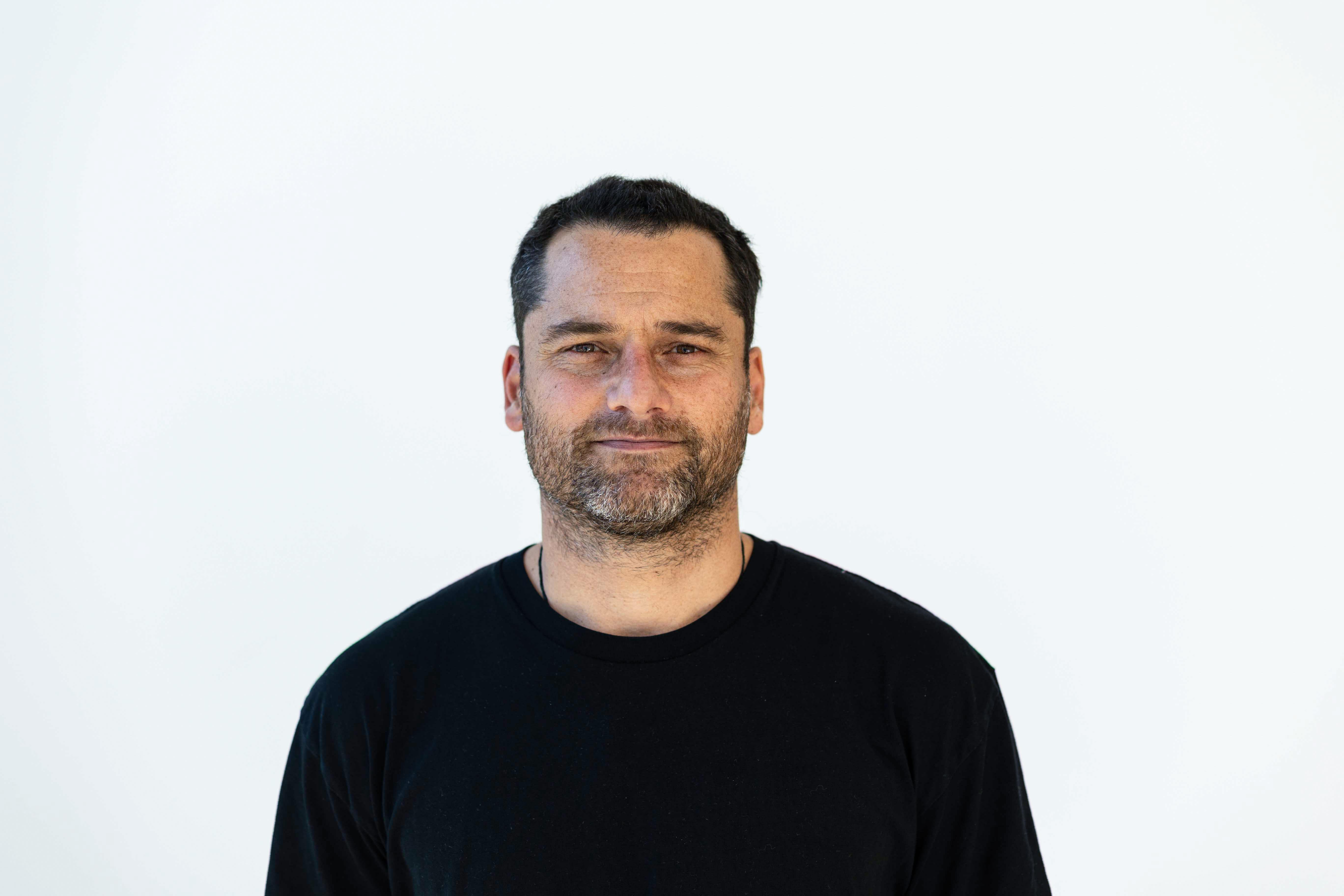 Black-and-white portrait of a smiling photographic artist based in Whāingaroa (Raglan), holding a camera, co-founder of Halide Studios, photographed in studio lighting