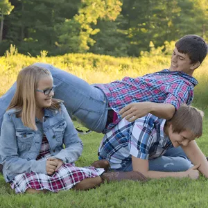 A playful pile-up between three adult siblings during a family photo shoot, capturing humor and closeness