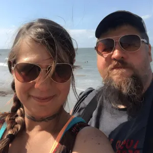 Chris and Dan smiling together on the beach, symbolizing the real-life connection and humor that inspire Chris’s couples work.