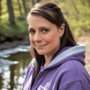 Chris Prebble, licensed therapist, wearing a purple hoodie and smiling softly by a calm creek
