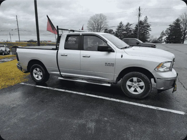 D&M Pilot Car Service silver Ram 1500 escort vehicle equipped with roof rack, safety flags, and signage parked in a lot before an oversize haul.