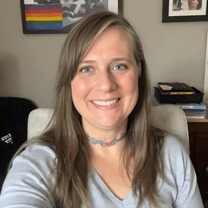 Chris Prebble, LPC, smiling warmly in her office, with a rainbow pride flag visible in the background.