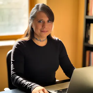 Chris Prebble, LPC, sitting at a desk with a laptop in a warmly lit home office with bookshelves