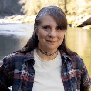 Christine Prebble, LPC, EMDR-trained therapist and apprentice in TF-EMDR in Central Pennsylvania, smiling beside a river in a plaid flannel shirt.