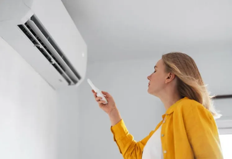 Homeowner adjusting wall-mounted AC unit with remote control during HVAC maintenance plan season