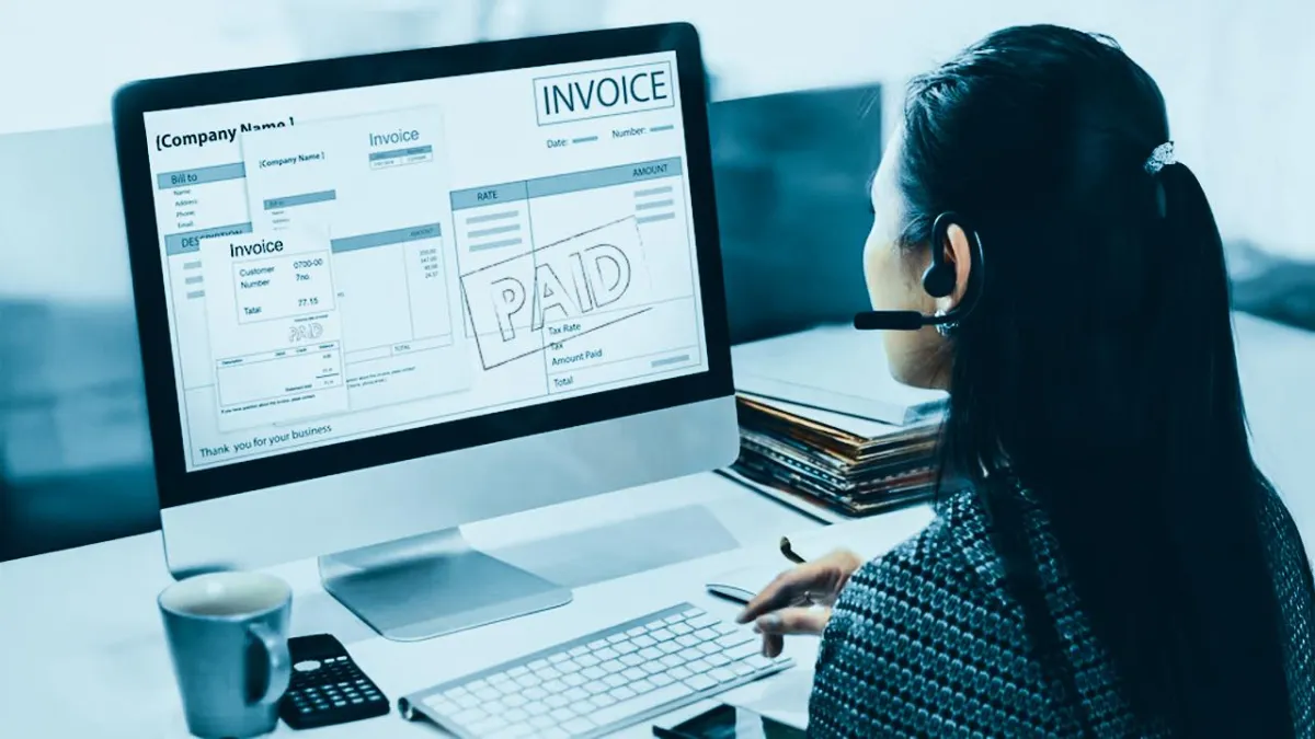 Woman wearing a headset at a computer displaying a paid invoice screen.