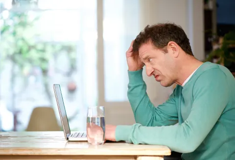 man in green shirt confused at a table with computer
