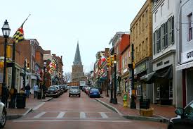 Historic downtown street with shops, brick buildings, and cars leading toward a church spire