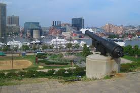 Overlook of a harbor with boats and skyscrapers, featuring a historic cannon monument in the foreground