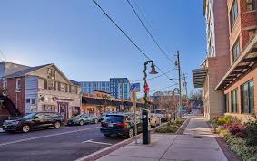 Street view of a small downtown area with shops, parked cars, and modern buildings in the background