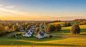 Aerial view of rolling countryside with farmhouses, open fields, and trees at sunset