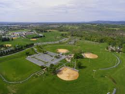 Aerial view of a large community park with multiple baseball fields, walking paths, and surrounding farmland