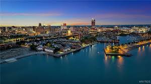 Aerial nighttime view of a brightly lit harbor with boats and downtown city skyline