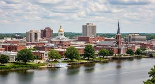 City skyline view across a river with historic buildings, church spires, and modern structures.