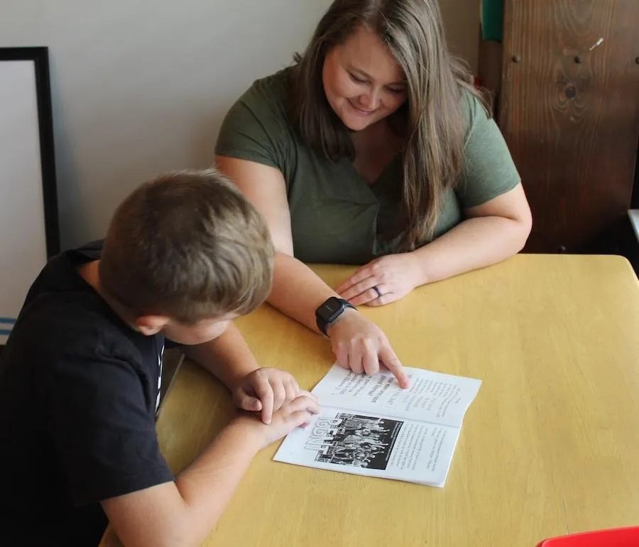 Cara Robertson tutoring an elementary student and pointing to a book