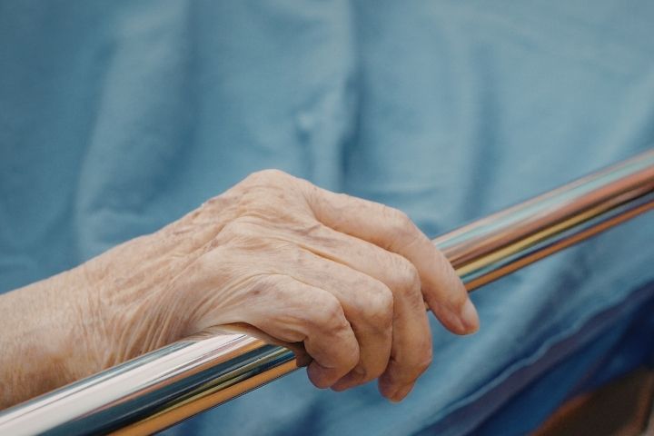A hand resting on the protective side barrier of hospital Bed rails.
