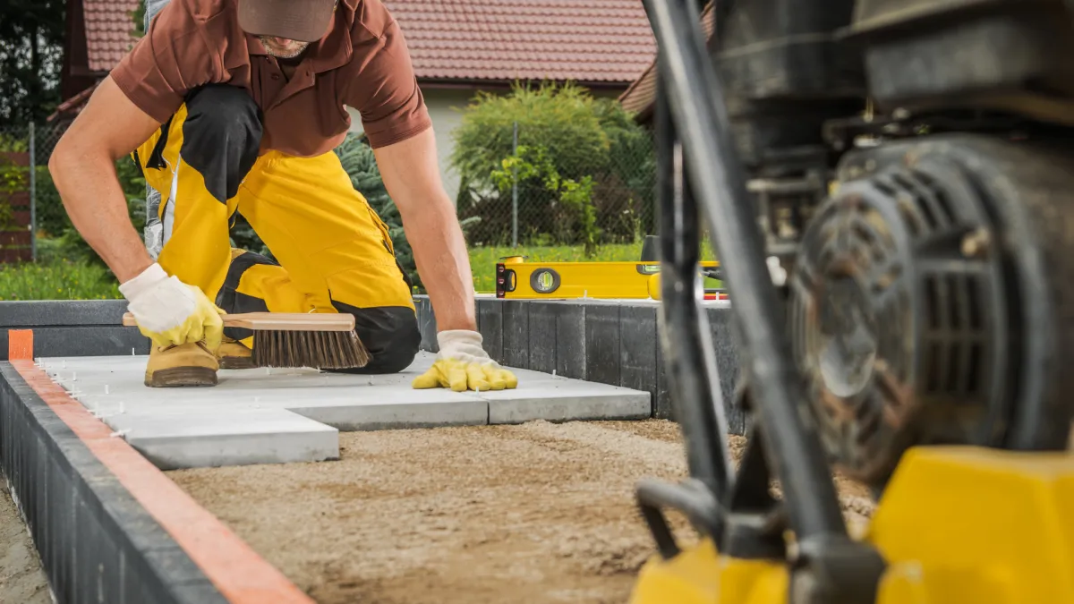 Worker setting down concrete pavers. 