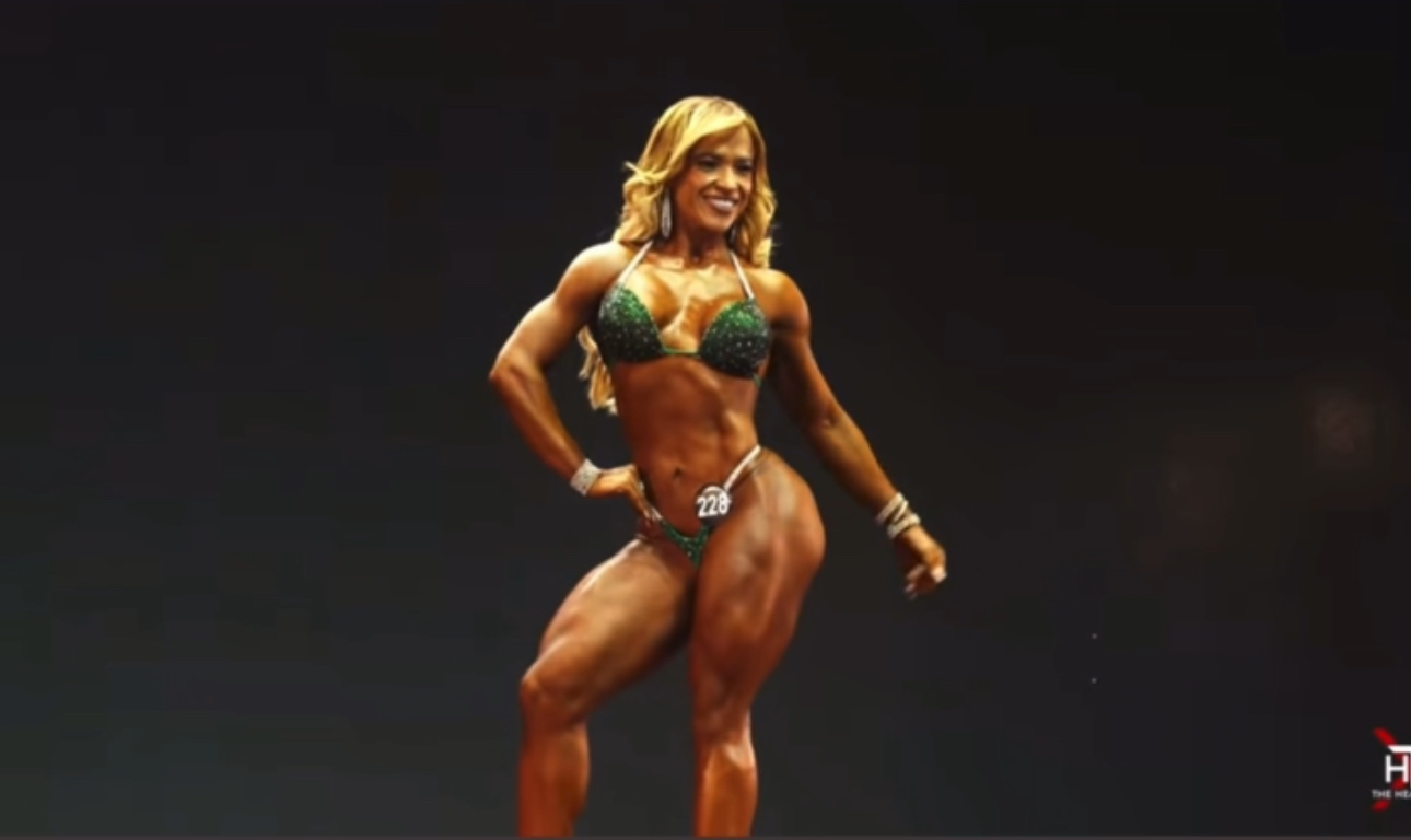 [NOMBRE DE LA ENTRENADORA] sonriendo, vestida con ropa deportiva, en un gimnasio moderno de Bogotá, con luz natural y ambiente profesional.