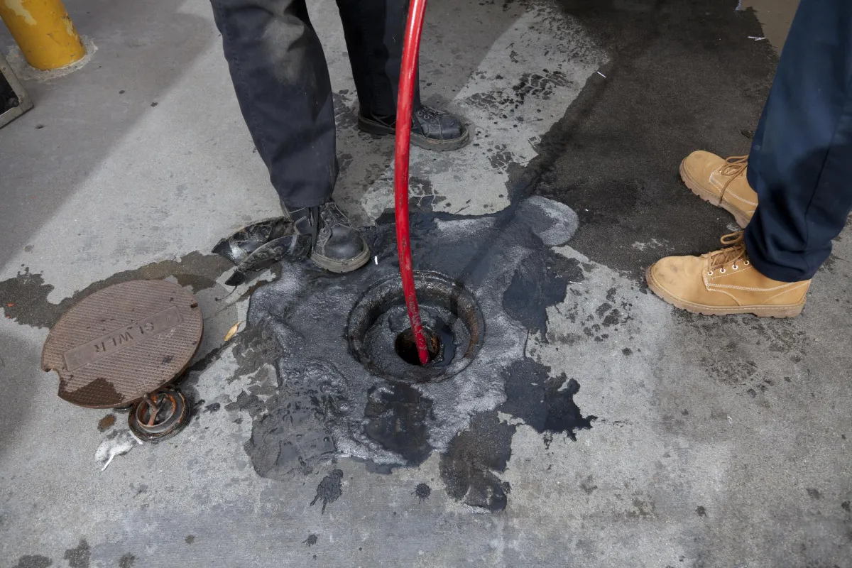 Technicians performing hydro jetting through a sewer access point.