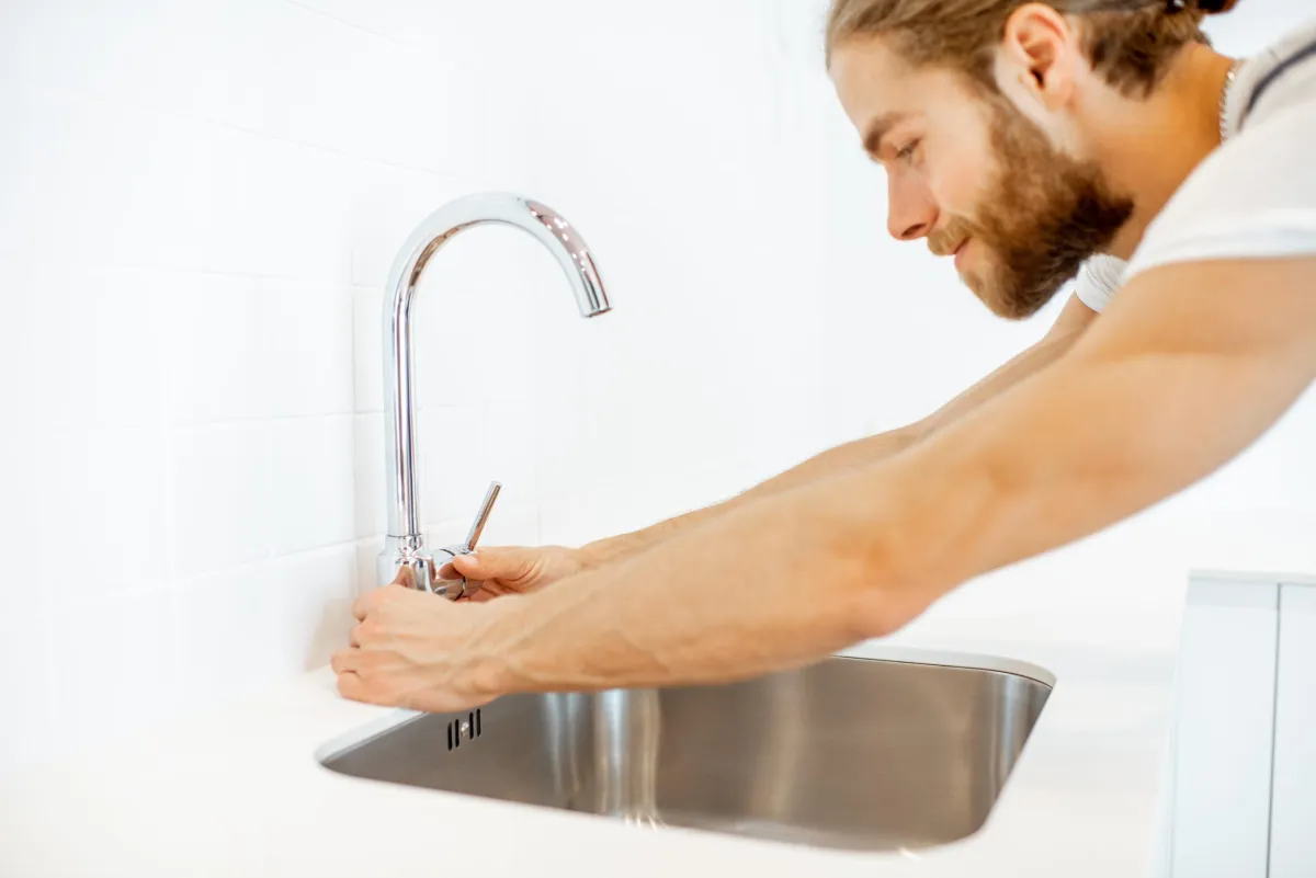 Man tightening a faucet on a stainless steel kitchen sink.