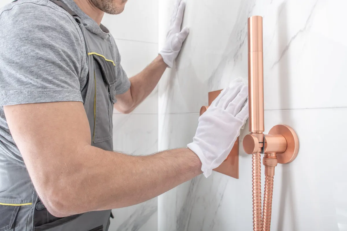 Technician installing copper piping in a tiled shower wall.