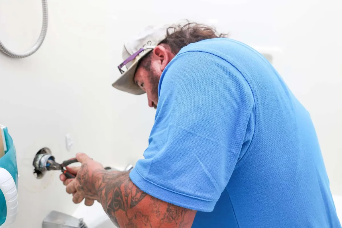 Plumber in blue shirt using a wrench to install or repair a wall-mounted water fixture.