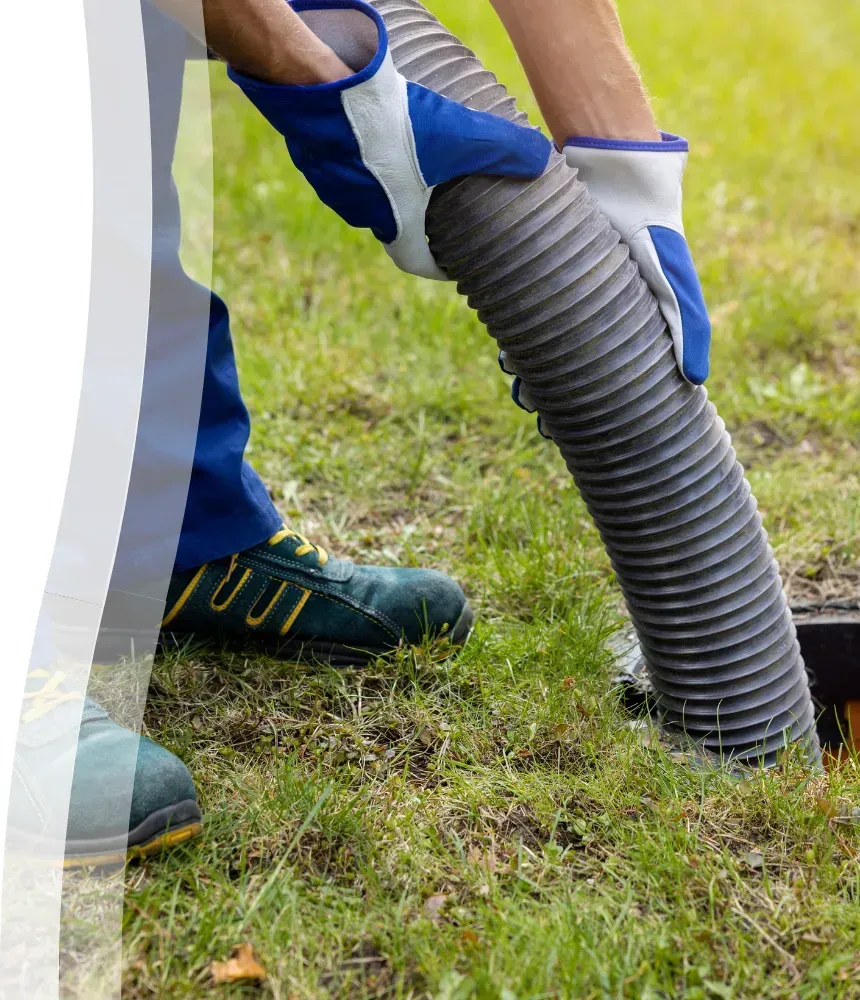 Technician using a vacuum hose to pump a residential septic tank in a grassy backyard.