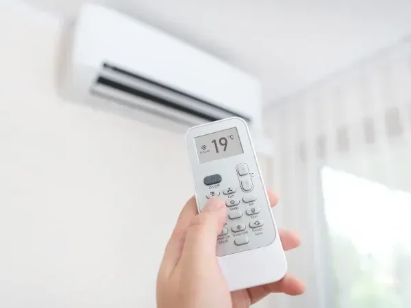 Hand adjusting air conditioner temperature with remote control.