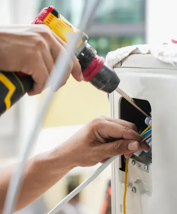 Technician using a power drill to install or repair an air conditioner unit.