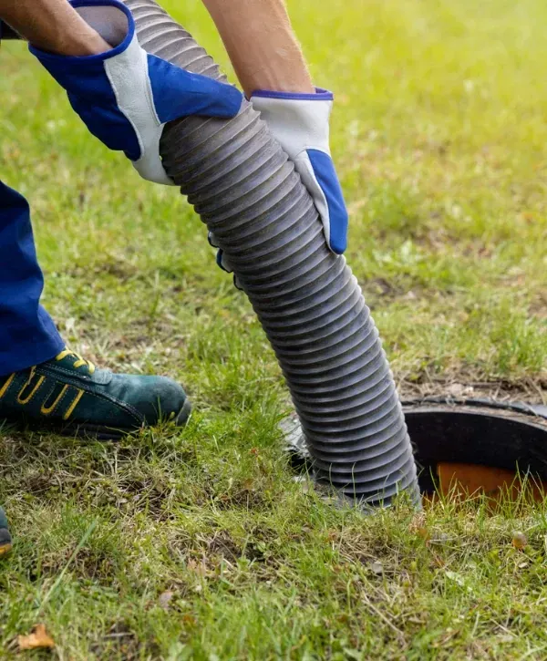 Technician inserting a vacuum hose for septic tank pumping on grass.