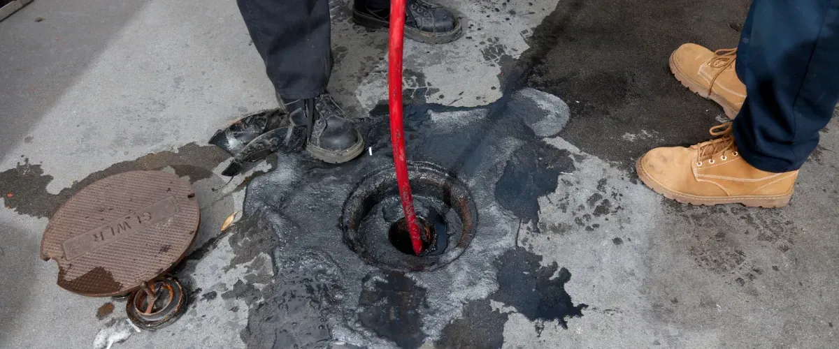 Workers cleaning a sewer line using industrial drain equipment.