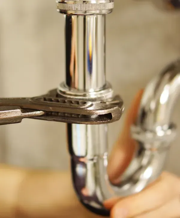 Plumber tightening a chrome pipe with a wrench under a sink