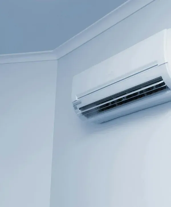 A white split-system air conditioner mounted high on a light blue wall, with the ceiling and corner visible.