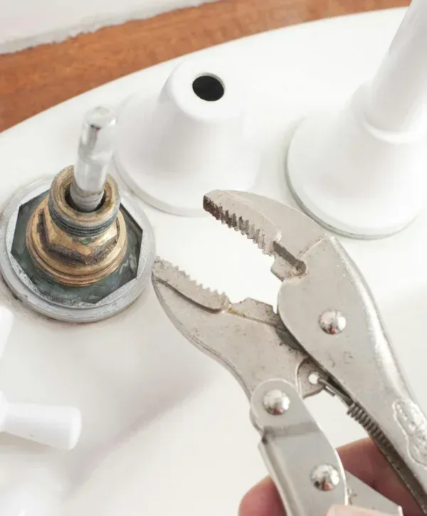 A male plumber fixing the pipes under a kitchen sink, sitting on the floor with his toolbox next to him.