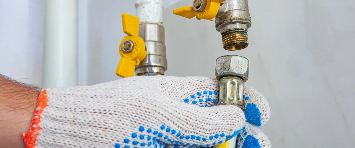 A gloved hand holds a pipe fitting to connect to a threaded valve, part of a plumbing system installation.