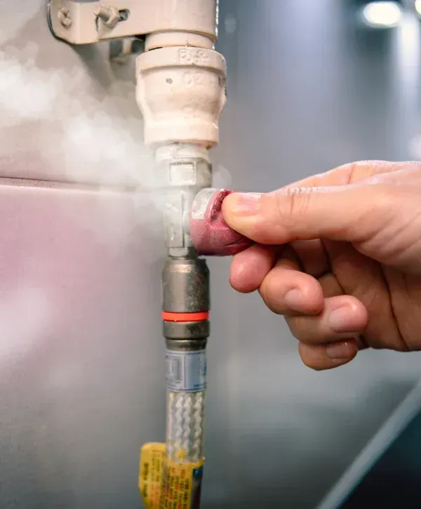 A hand adjusts a red valve on a steaming pipe, indicating a gas or water leak in an industrial setting.