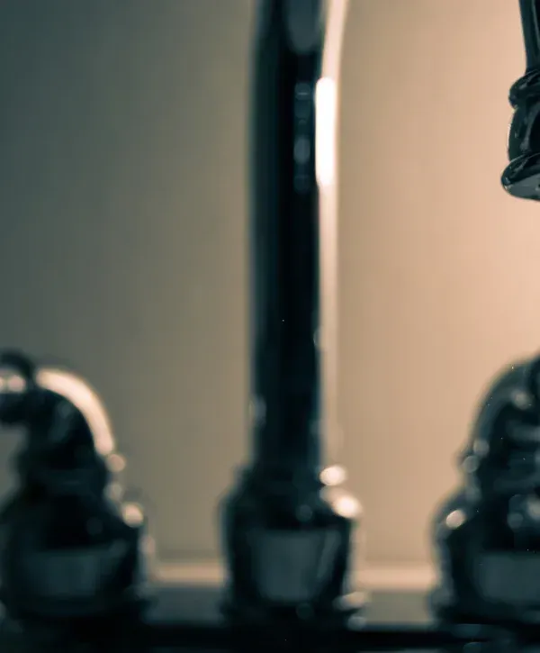 A close-up, highly blurred perspective of shiny metal kitchen faucet handles and spout against a muted background.