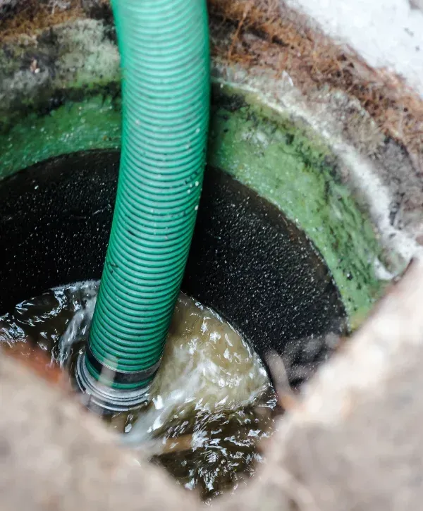 A vibrant green ribbed hose descends into a dark, murky well, actively pumping out cloudy, brown water.