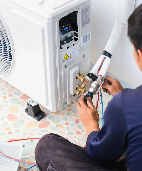 A technician wearing a blue shirt is installing an air conditioner unit on a colorful tiled floor.