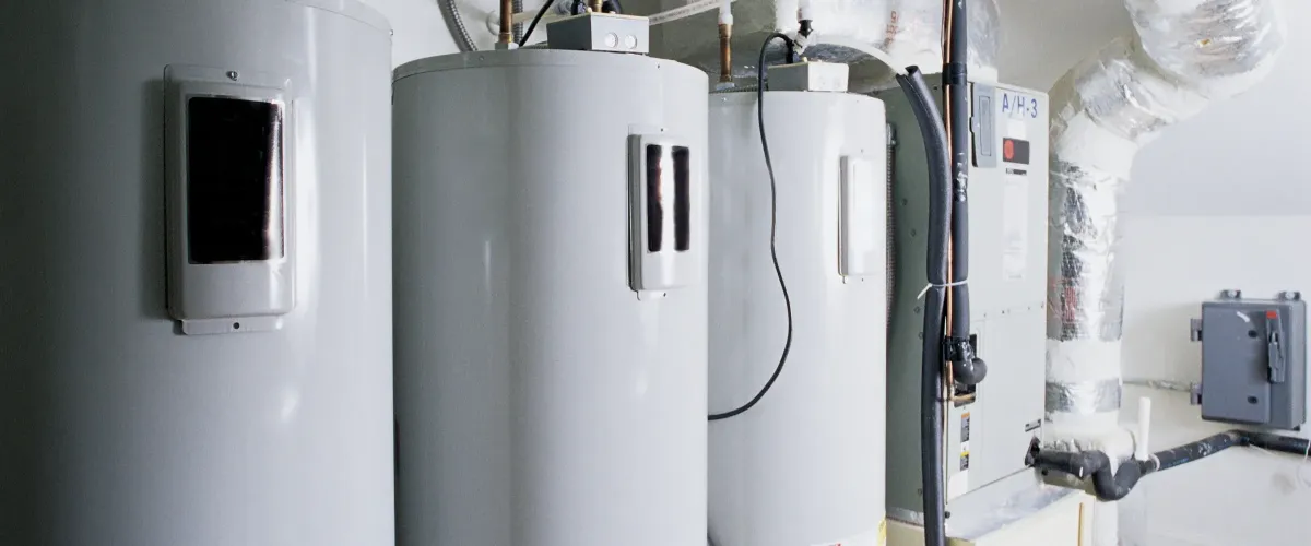 Three industrial-sized water heaters and an HVAC unit with ductwork in a utility room.