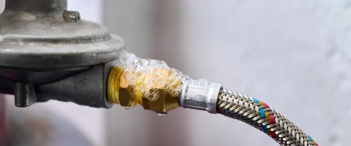 Soap bubbles forming on a brass gas fitting connected to a braided hose, indicating a gas leak.