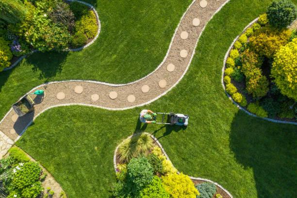 Bird’s eye view of a green lawn with stone paver stepping stones, manicured landscaping, bushes, trees, and a man mowing the lawn.