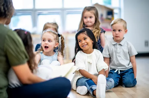 Girl folds paper while watching teacher on laptop