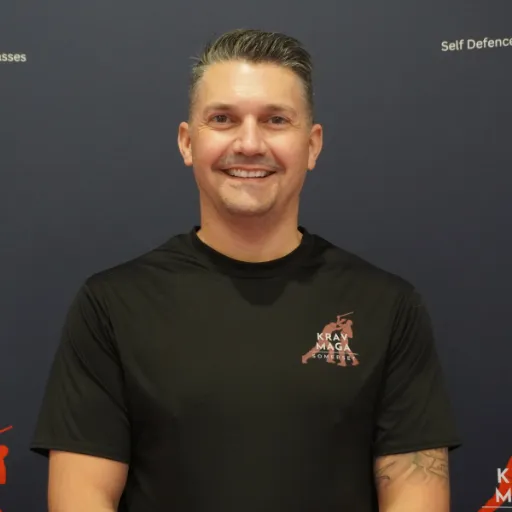 Male instructor, early 40s, leading a group drill, muscular build, friendly expression, diverse students in background, 1:1 aspect ratio