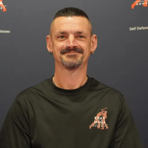 Male instructor, early 40s, leading a group drill, muscular build, friendly expression, diverse students in background, 1:1 aspect ratio