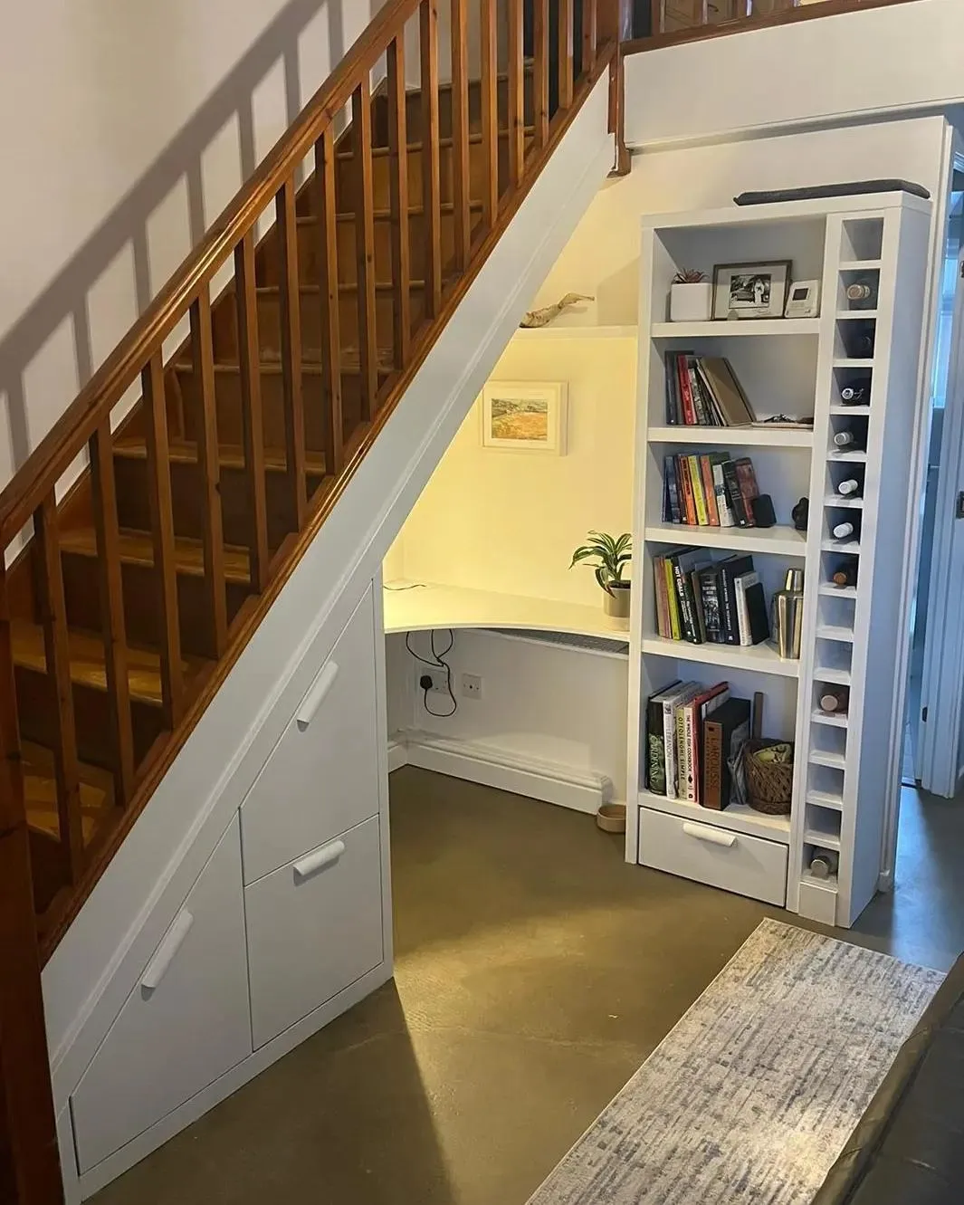 Smart under-stair storage solution with a built-in white desk and bookshelves, custom-crafted by a West Midlands joinery expert, featuring clean lines and efficient use of space, with practical cupboards and display shelves to organize books and decor, enhancing the functionality of a UK home's entryway.